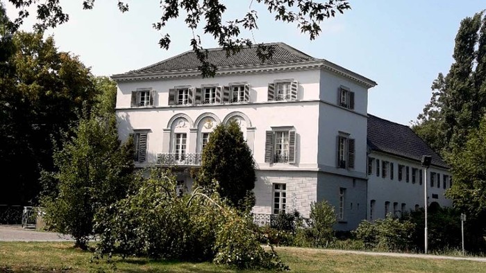 Elegante zweistöckige Villa, umgeben von üppigem Grün unter klarem Himmel.