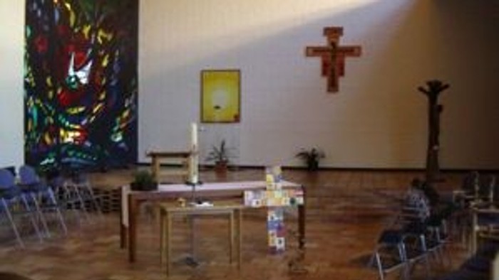 Eine friedvolle Kapelle zeigt religiöse Kunst, ein Kreuz, einen Altartisch mit Kerzen und schlichte Holzstühle.