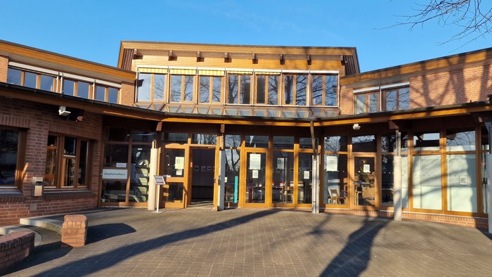 Das Bild zeigt ein modernes Gebäude mit großen Fenstern und einem überdachten Eingangsbereich.