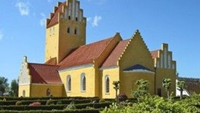 Lysende gul kirke med rødt tag og højt spir mod en klar blå himmel.