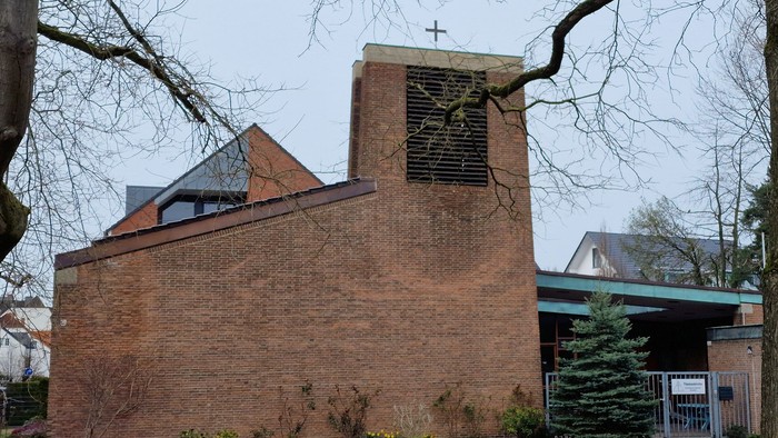 Ein Ziegelgebäude mit Uhrturm und Kreuz, umgeben von Bäumen und Büschen