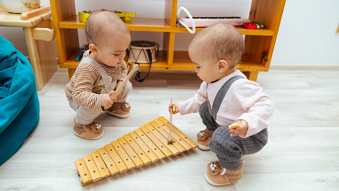 Zwei Babys spielen mit einem Holz-Xylophon in einem kindgerechten Indoor-Spielbereich.