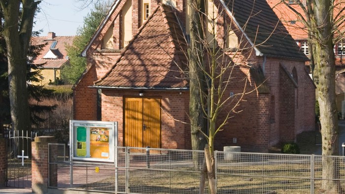 Historische Backsteinkirche mit steilem Satteldach und Holztür, umgeben von kahlen Bäumen.