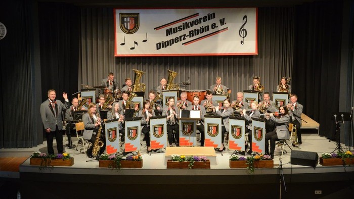 Ein Orchester tritt auf einer Bühne auf, begleitet von einem Mann, der spricht