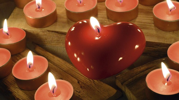Herzförmige Kerze umgeben von vielen kleinen brennenden Kerzen