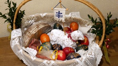 Traditioneller Osterkorb gefüllt mit bemalten Eiern, Brot, Obst und Dekorationsartikeln.
