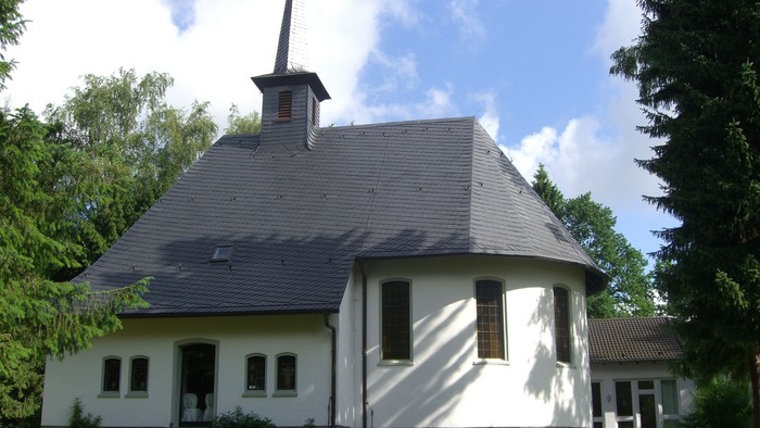 Weißes Haus mit schwarzem Dach und Turm, umgeben von Bäumen