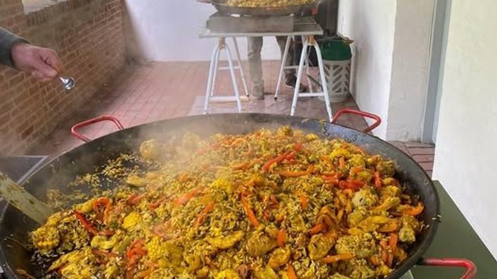 Stor paellapande fyldt med farverigt skaldyr og ris, der tilberedes udendørs.