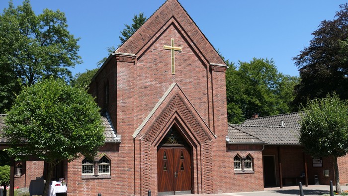 Die Kirche aus Ziegelsteinen mit Kreuz darüber und Bäumen drumherum