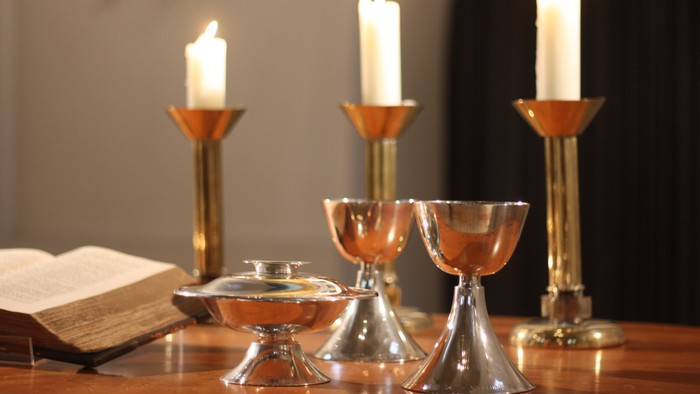 Drei brennende Kerzen auf Ständern und zwei silberne Schalen auf einem Holztisch