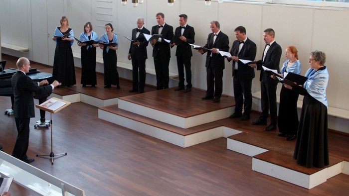 Ein Chor proben in einem Raum mit Klavier und großen Fenstern.