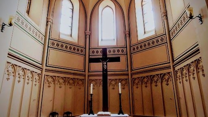 Eleganter Kirchenaltarbereich mit gewölbten Buntglasfenstern und einem von Kerzen beleuchteten Kruzifix.