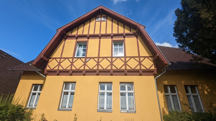 Ein gelbes, zweistöckiges Haus mit braunem Holzfachwerk und weißen Fenstern unter einem klaren blauen Himmel.