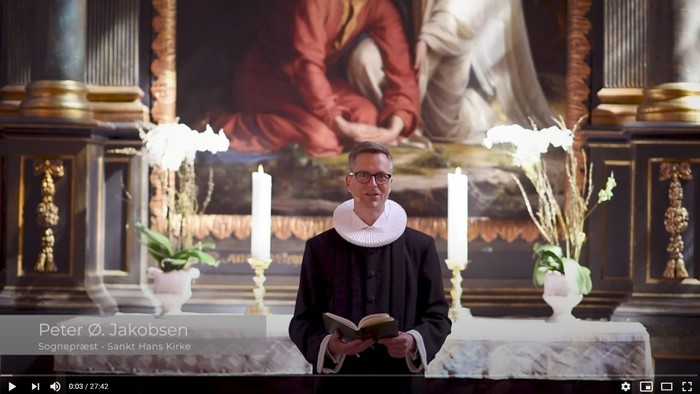 Mand i svart kapittel i kirke med bog og blomsterstokke.