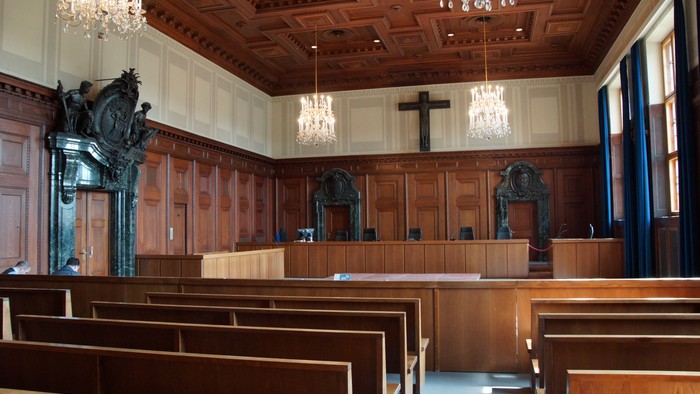 Eleganter Gerichtssaal mit Holzbänken, Richtertisch und prunkvollen Kronleuchtern mit zentraler Kreuzverzierung.