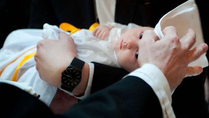Et barn bliver døbt, mens hænder holder og velsigner barnet under en ceremoni.