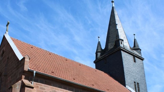Kirche mit hohem Turmspitz und Bank davor.