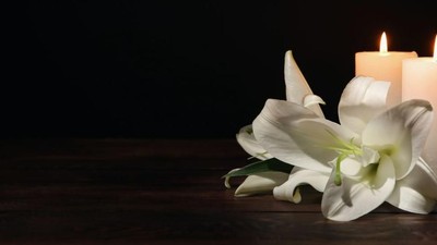 Elegante weiße Lilien flankieren zwei brennende Kerzen auf einer dunklen Holzoberfläche und schaffen eine ruhige Atmosphäre.