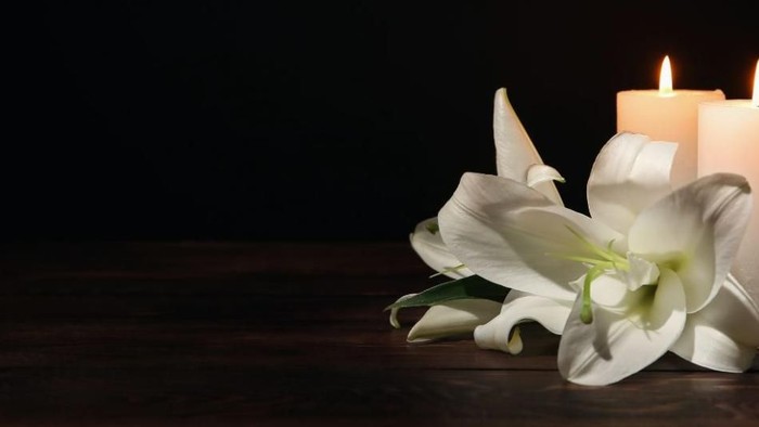Elegante weiße Lilien flankieren zwei brennende Kerzen auf einer dunklen Holzoberfläche und schaffen eine ruhige Atmosphäre.