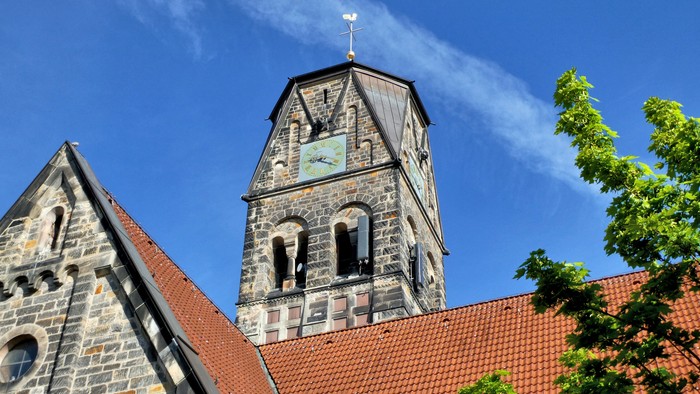 Historische Steinkirche mit hohem Uhrturm und rotem Ziegeldach unter einem klaren blauen Himmel.