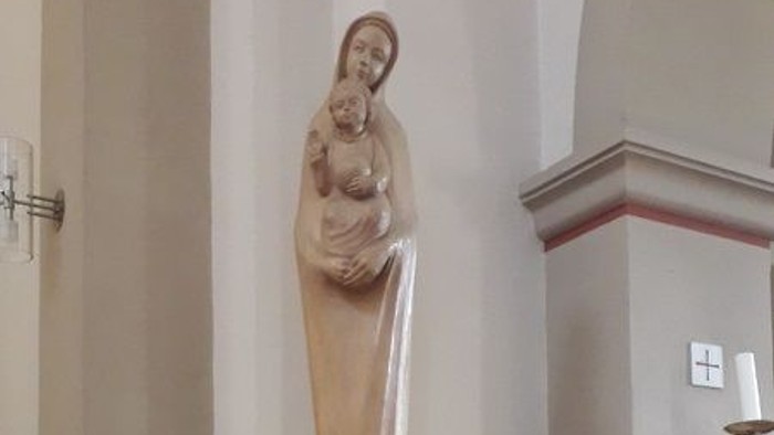 Eine Statue der Jungfrau Maria mit Baby Jesus in einer Kirche, umgeben von Blumen und Kerzen.