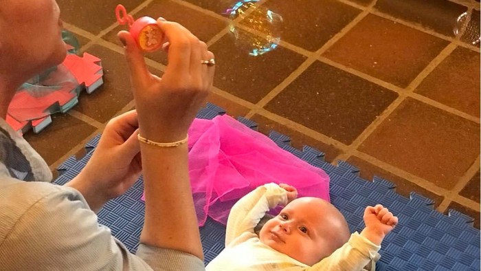 En mand spiller bobleblæser for et barn på en blå matte.