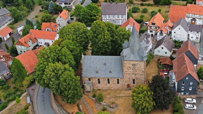 Luftaufnahme eines malerischen Dorfes mit einer historischen Kirche, umgeben von bunten Häusern und üppigem Grün.