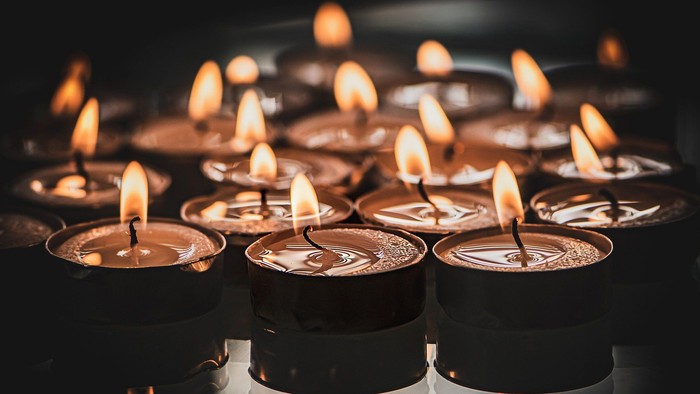 Mehrere brennende Kerzen in Metallhaltern, dunkle Umgebung