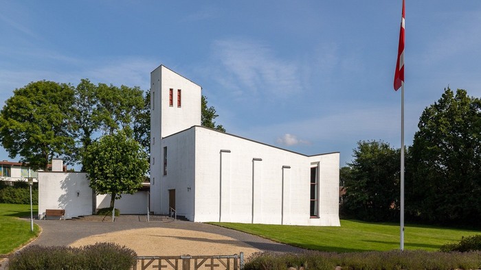 Et hvidt moderne kirkebygning med en flagstang med rødt flag foran