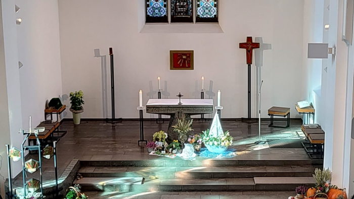 Ein geschmückter Altar in einer Kirche mit Blumen, Kerzen und einem Kreuz.