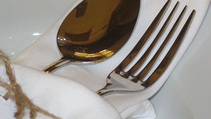 Elegant sølvbestik pakket ind i en serviet med en dekorativ sløjfe som accent.