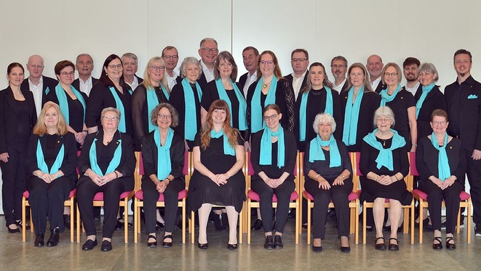 En korgruppe i matchende sorte dragter med turkisfarvede bånd poser sammen i to rækker.