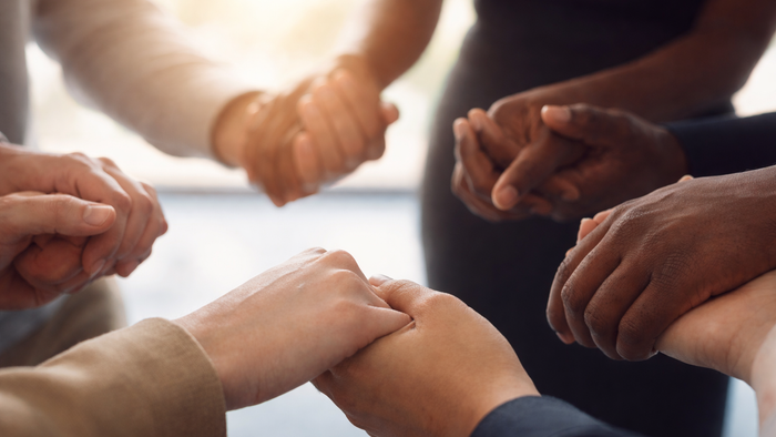 Eine Gruppe von Menschen, die sich an den Händen halten und einen unterstützenden, verbundenen Kreis bilden.