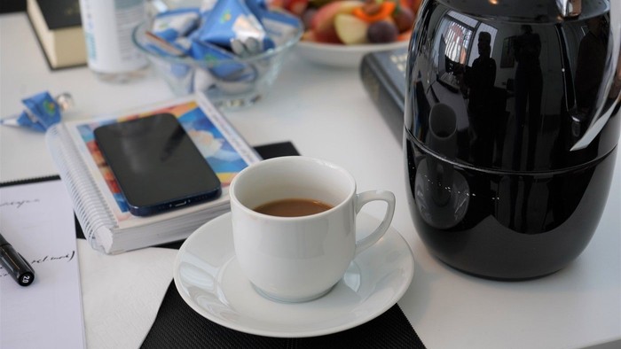 En skrivebord med kaffe, bog, mobiltelefon og mad.