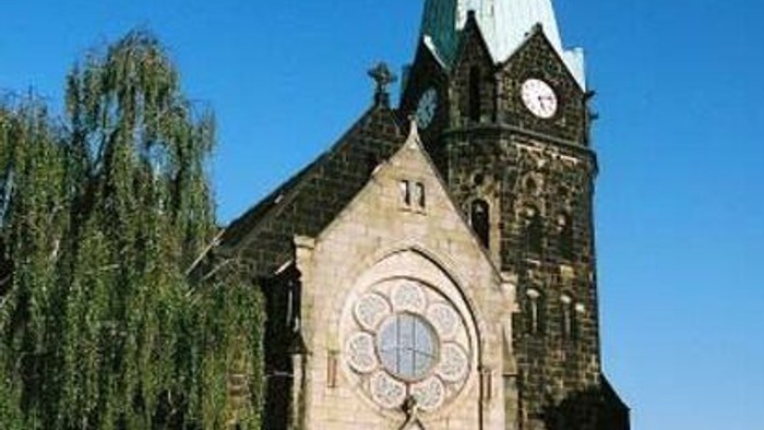 Gotische Kirche mit hohem Turm, rundem Buntglasfenster und Uhrturm vor klarem Himmel.