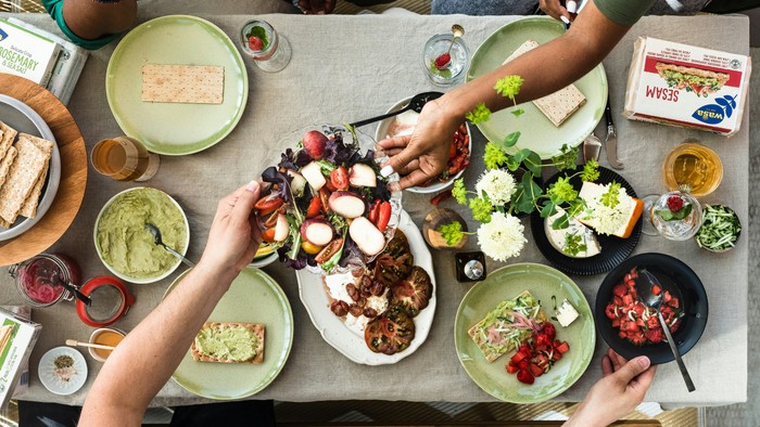 Eine Gruppe von Menschen genießt ein gemeinsames Essen mit verschiedenen Gerichten und Snacks auf einem Tisch.