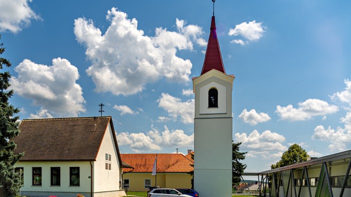 Eine Kirche mit einem hohen Kirchturm und einem in der Nähe geparkten Auto unter einem blauen Himmel mit weißen Wolken.