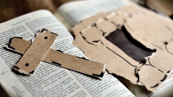Auf einer aufgeschlagenen Bibel liegt ein Pappkreuz