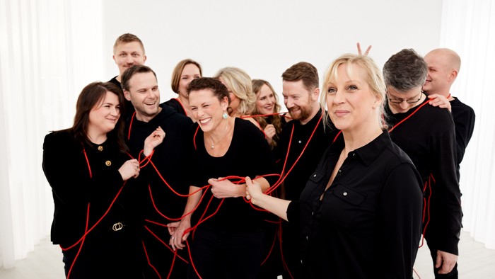 En gruppe mennesker flettes legende sammen med røde snore, mens de poserer i formelt sort tøj.
