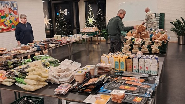 En festlig madmarkedopsætning med forskellige pakkede varer, snacks og mennesker, der organiserer ting på borde.