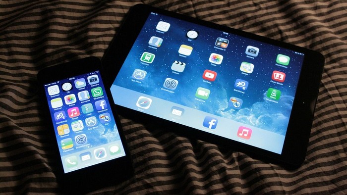 Zwei Apple-Geräte – ein Smartphone und ein Tablet – zeigen ihre Startbildschirme nebeneinander auf einer gemusterten Oberfläche.