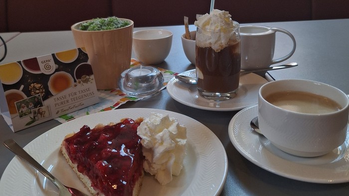 Ein gemütliches Tischgedeck mit einem Stück Beerenkuchen, Kaffeegetränken und einer Portion Edamame in einem Café.