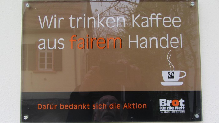 Ein Schild, das fair gehandelten Kaffee mit einer Kaffeetassengrafik bewirbt und einer Aktionsgruppe dankt.