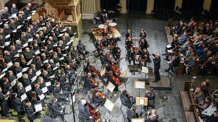 Ein großer Konzertsaal mit Orchester und Chor auf der Bühne, Zuschauer im Hintergrund