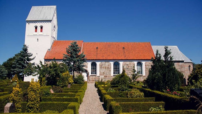 En smuk kirke med rødt tag og en have med formede buske og træer.