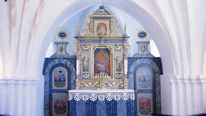 En prægtig altertavle i en kirke med detaljerede malerier og gulddekor.