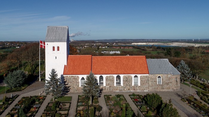 En lille kirke med rosengård og udsigt over landskabet