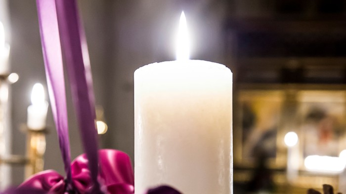 Hvidt bloklys i adventskrans med lilla bånd.