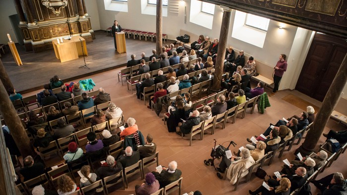 Eine überfüllte Gottesdienst mit Teilnehmern, die in Reihen sitzen und aufmerksam dem Redner vorne zuhören.