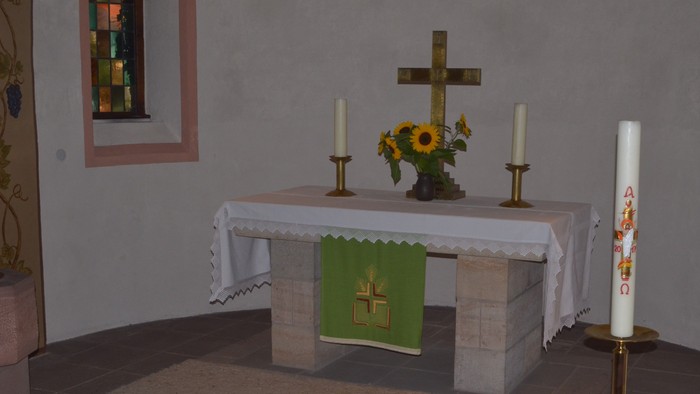 Eine friedvolle Altargestaltung mit einem Kreuz, Kerzen, Blumen und einem grünen Tuch mit einem Kreuzemblem.